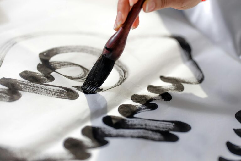 Close-up of a hand using a calligraphy brush to apply black ink on white paper.